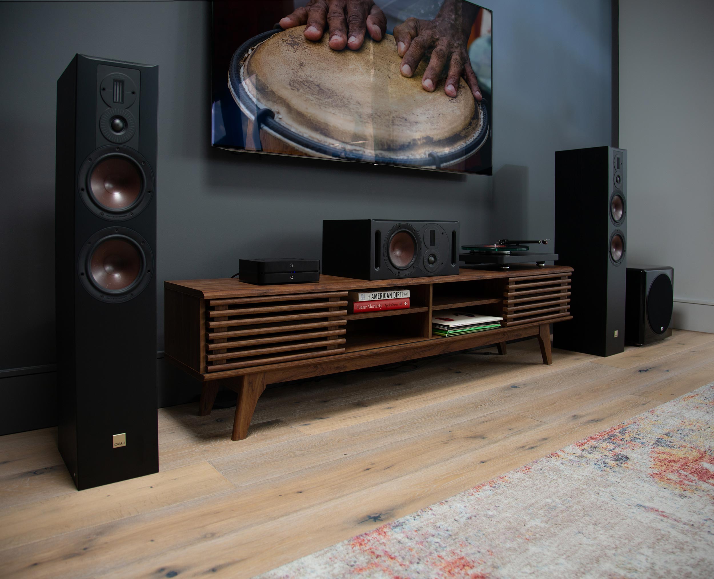 Two black tower speakers and a center channel speaker on a wooden credenza