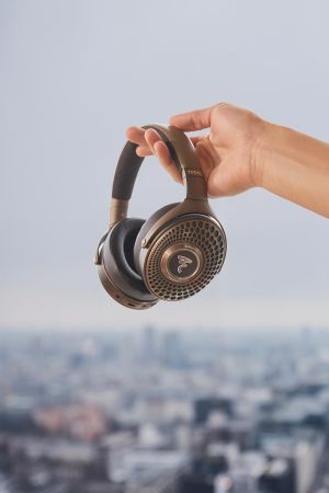 Hand holding black Focal headphones above cityscape