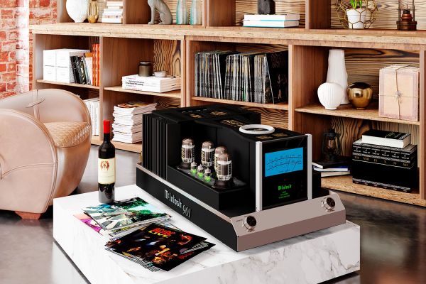 A stylish living room with a McIntosh 901 amplifier prominently displayed on a low table. Surrounding the amplifier are vinyl records, books, and decorative items. The background features wooden shelves and a mix of modern and vintage decor.