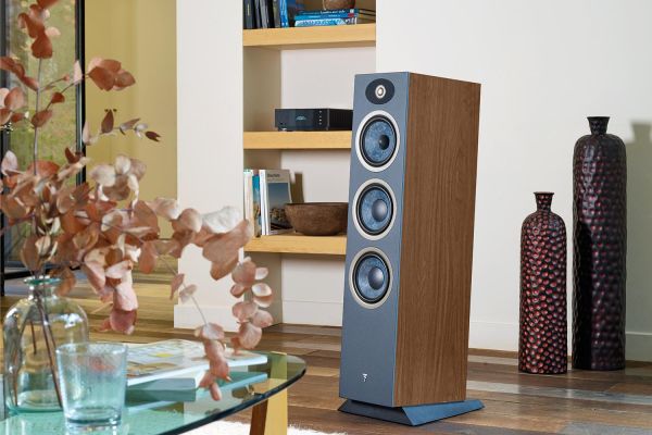 A living room featuring a Focal speaker with a wooden finish. The speaker stands on the floor near a built-in bookshelf filled with books and decorative items, including large vases.