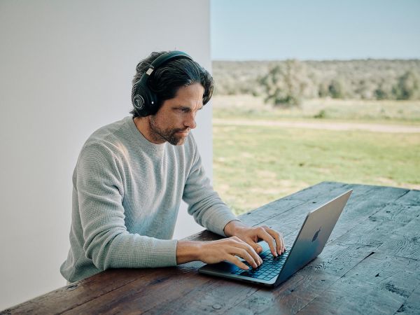 Man using laptop outdoors while wearing headphones