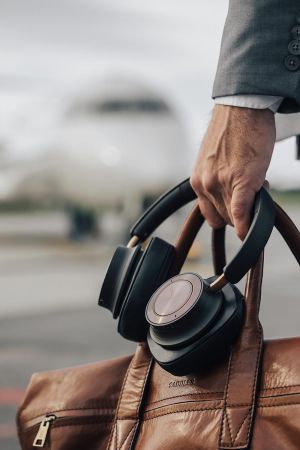 Hand holding black headphones hooked on a brown leather bag near an airport