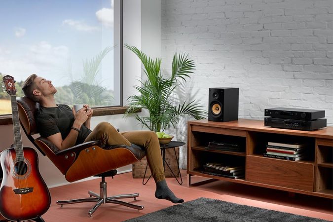 Man relaxing in a chair with a mug near audio equipment on a wood console