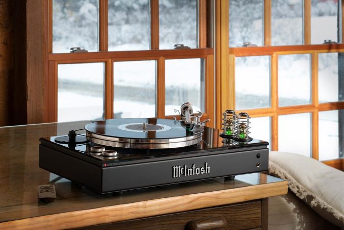 A vinyl record player placed on a wooden desk with a winter landscape visible through the large windows in the background.