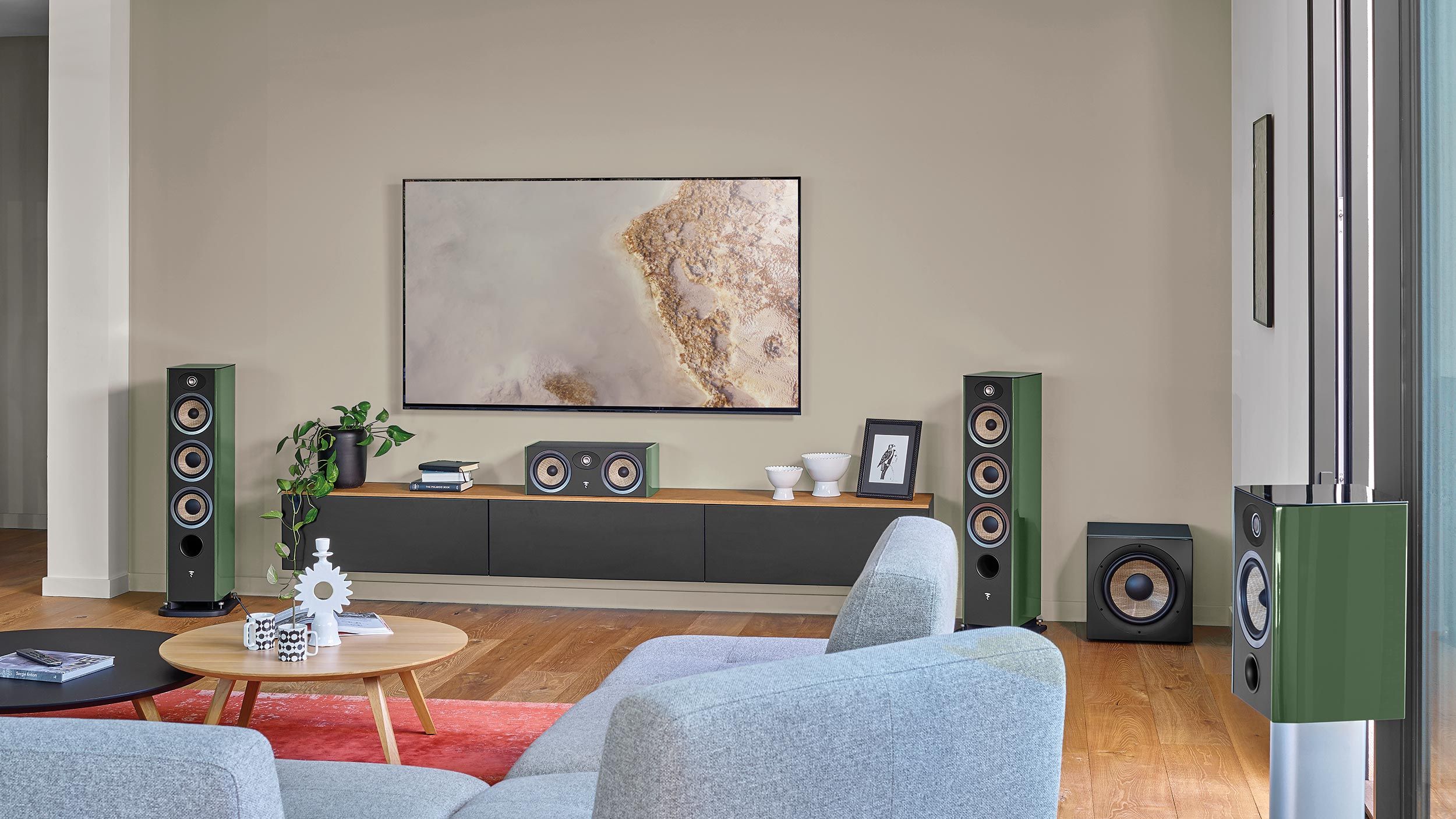Focal Evo X speakears setup in a modern living room with sleek, green speakers, a large wall-mounted TV, and minimalist decor.