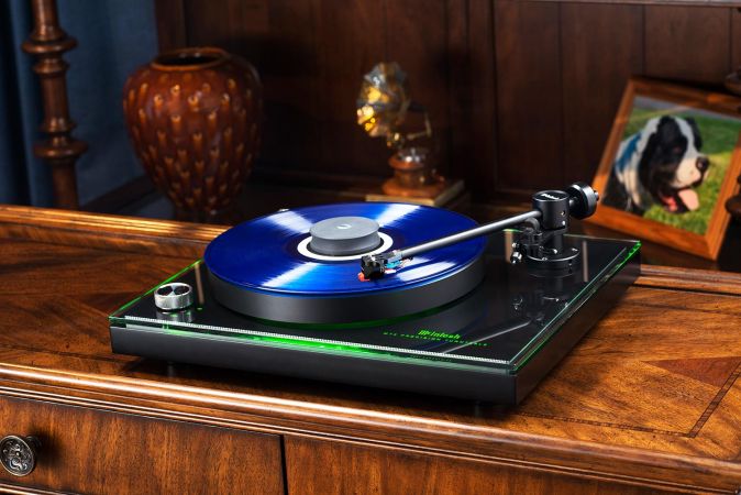 A record player with a vibrant blue vinyl spinning on a wooden surface, framed by vintage decor and a framed photo of a dog.