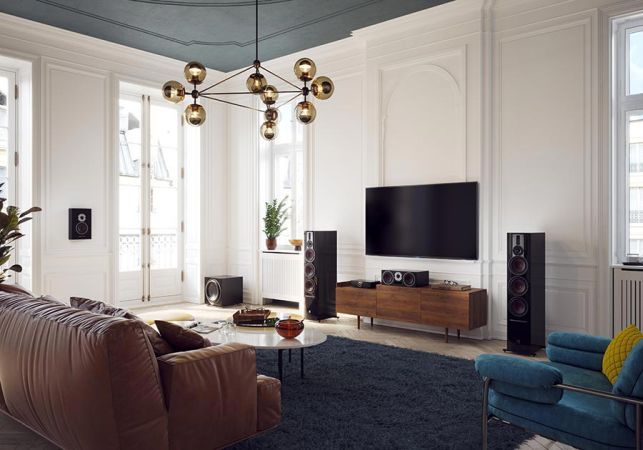 A stylish living room with a large flat-screen TV, floor-standing speakers, and a contemporary chandelier, creating a high-end audio-visual setup.