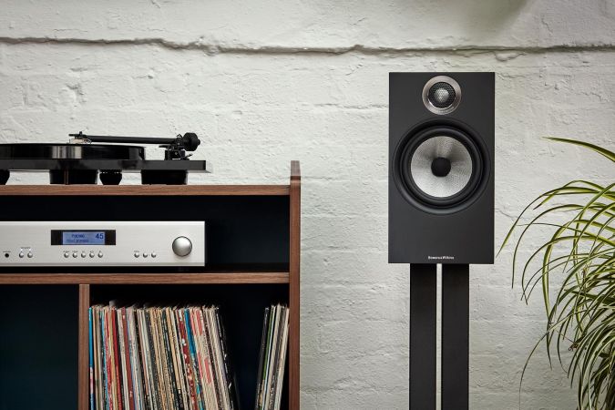 A minimalist audio setup with a compact speaker next to a turntable and a neatly arranged collection of vinyl records on a wooden shelf.